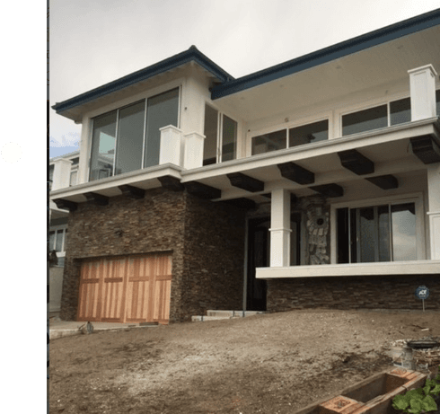 Modern two-story house featuring stone walls, wooden garage door, and large glass windows.