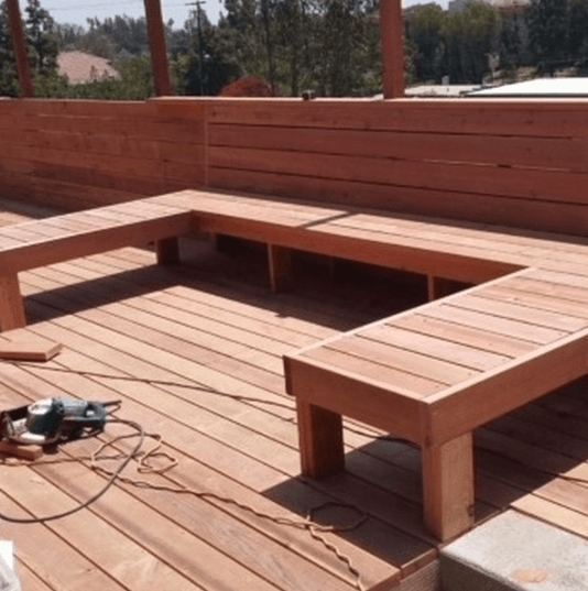 Custom U-shaped wooden bench under construction on a rooftop deck with a circular saw.
